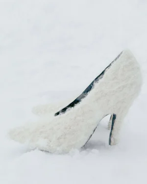 Pair of textured fuzzy off-white high heel pumps with pointed toes resting in fresh snow.