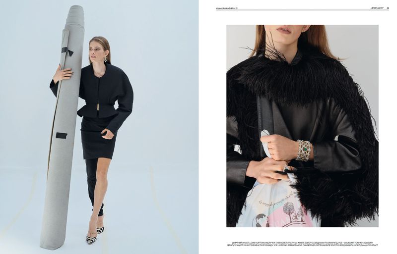 Fashion editorial shot of a woman holding a carpet, wearing a black skirt suit and heels on a white backdrop in a photography studio.
