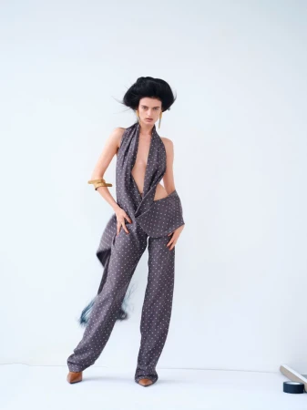 Fashion model poses in a polka dot patterned suit in front of a plain white background in a studio. Hair and clothes are styled.