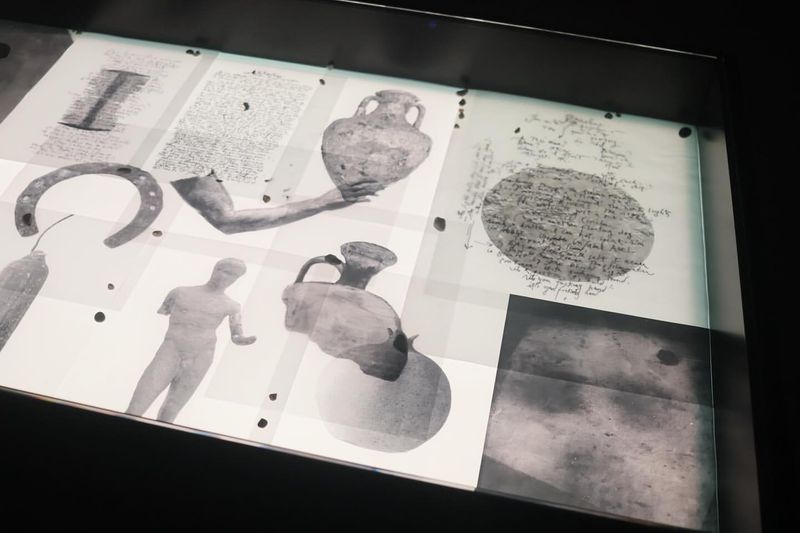 Display case showcasing artifacts including pottery shards, a horseshoe, sculpture fragments, and handwritten documents in black and white.