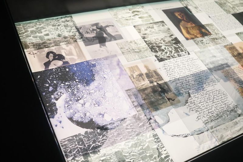 Artistic collage with layered photographs, handwriting samples, and watercolor textures on a glossy surface, rendered in monochrome tones.