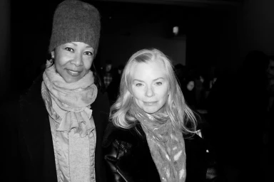 Black and white portrait of two women wearing winter coats and scarves standing together indoors