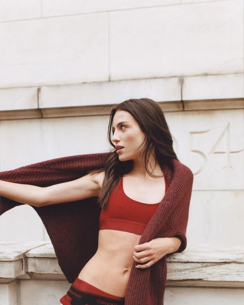Madeline Argy wearing red Calvin Klein underwear and a burgundy knit wrap against stone architecture.