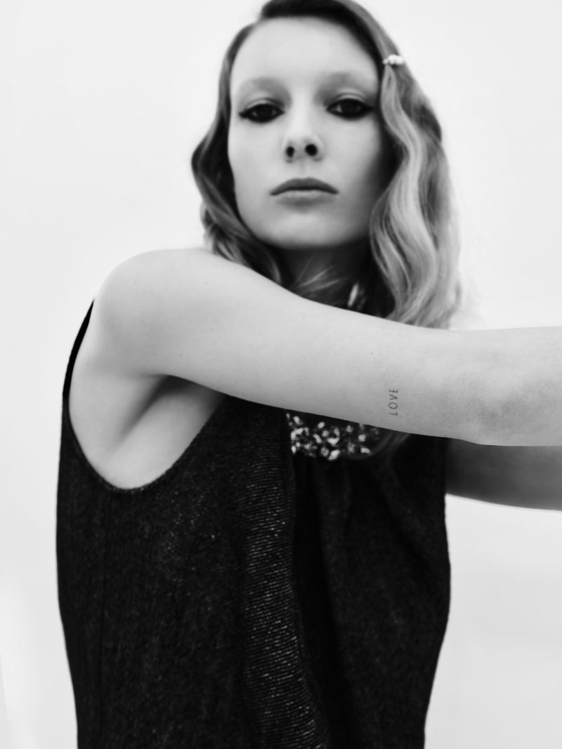 Black and white portrait of an adult woman with dark eye makeup, retro hairstyle, and a sleeveless black top against a white backdrop.