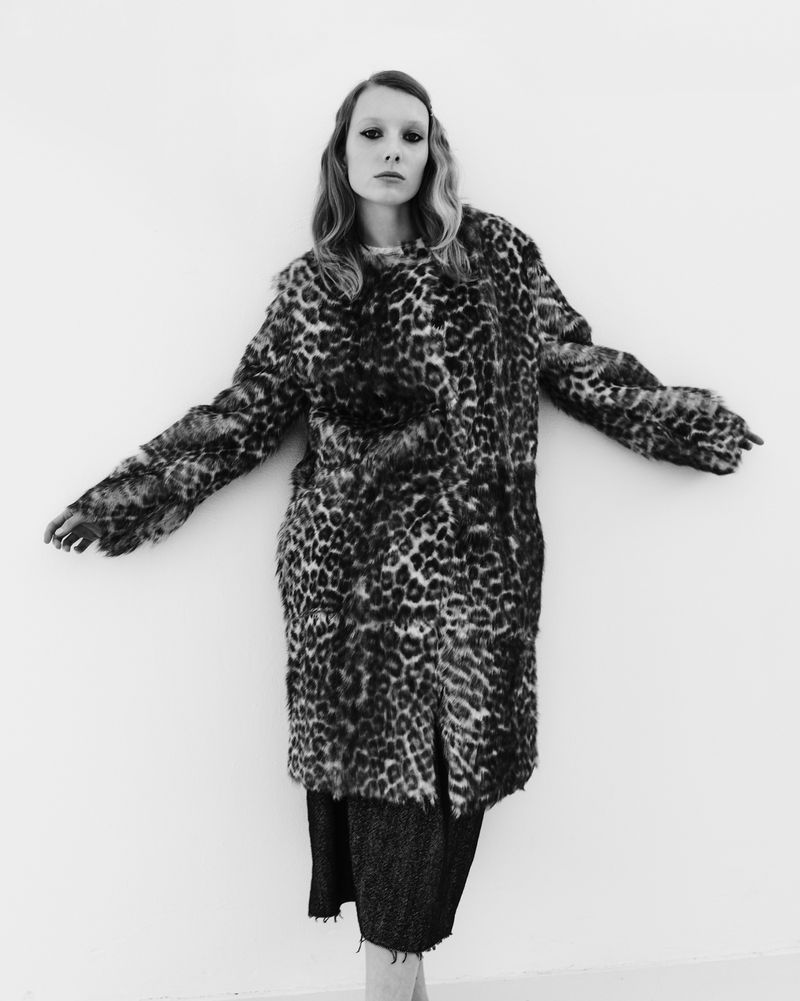 Model in a patterned leopard coat posing against a plain white studio background