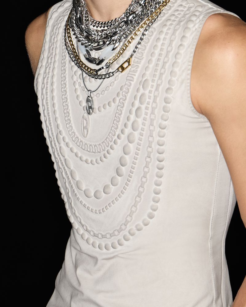 White top with layered necklaces, fashion-forward sleeveless design, and layered chain details against a dark backdrop. 