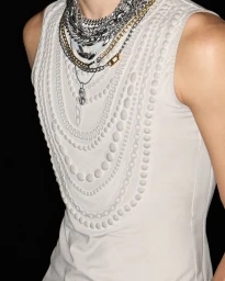 Close-up portrait of a model wearing an off-white textured tank top layered with chunky silver and gold chain necklaces.