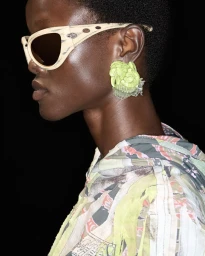 Close-up profile of a black woman wearing light-colored patterned sunglasses and a bright green floral earring for Diesel SS25.