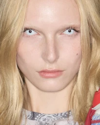 Close-up portrait of a blonde model with striking white contact lenses wearing patterned clothing for Diesel SS25.
