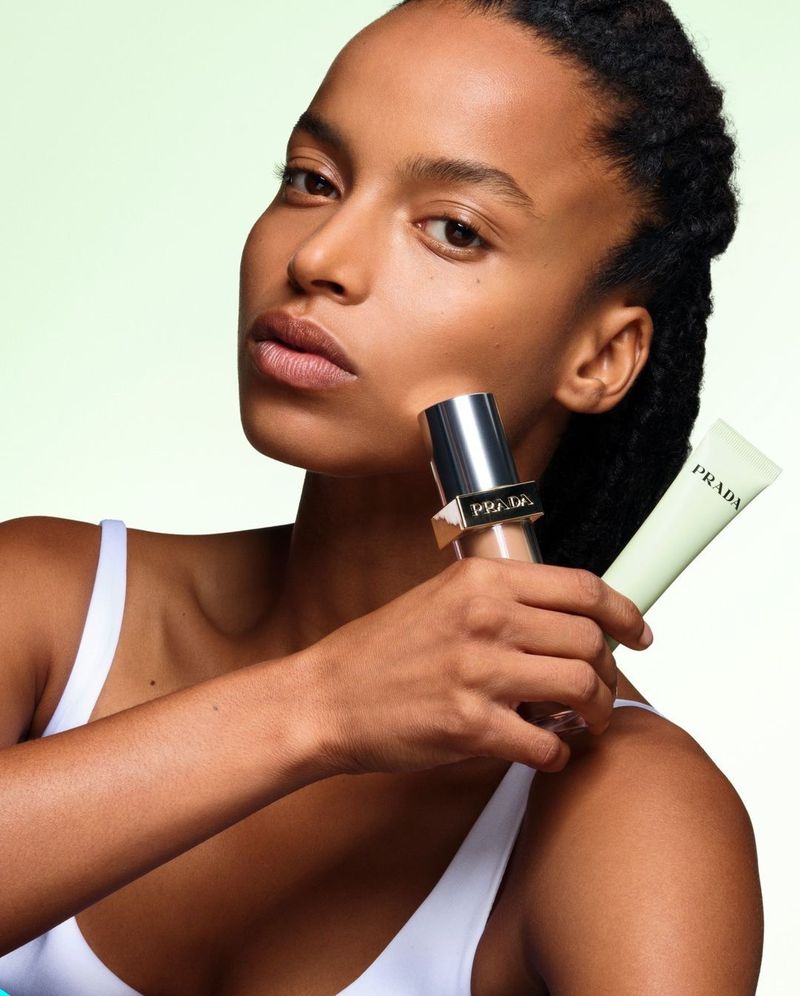 Beauty shot featuring a woman with tan skin holding Prada beauty products in front of a light green background, fashion and cosmetics.