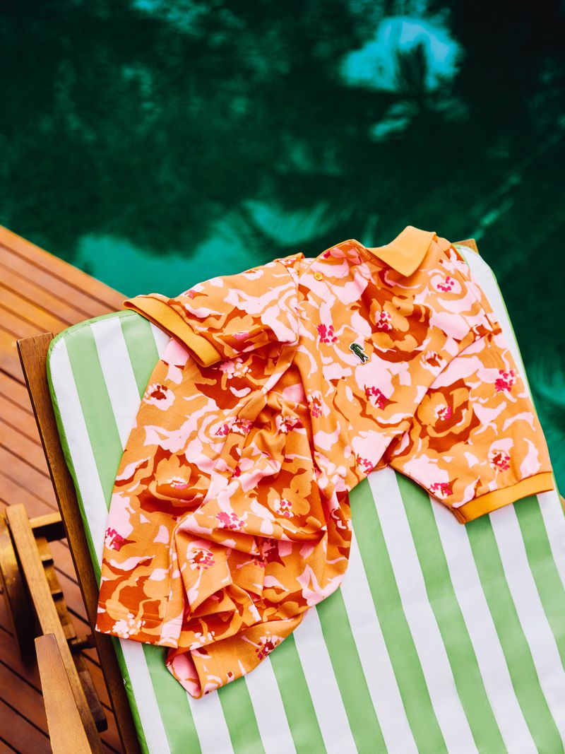 Orange and pink floral polo shirt casually draped on a green and white striped deckchair next to a wooden deck and green water.