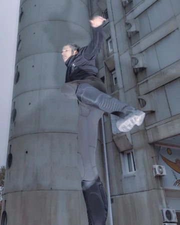 Male urban acrobat performs parkour stunt on city building, wearing activewear, with a modern architectural backdrop and overcast sky.
