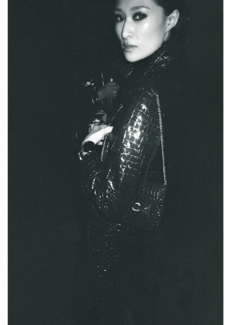 Monochrome portrait of an Asian woman wearing a glossy black jacket with a silver chain strap bag, posing in an indoor setting.