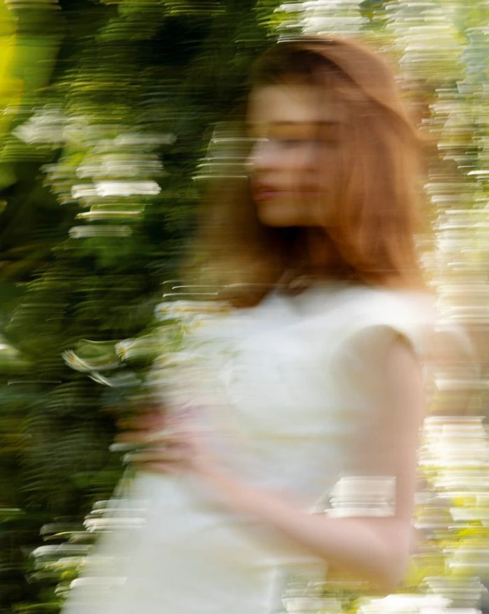 Ever Gabo Anderson in a white dress holding daisies with motion blur against a green foliage background