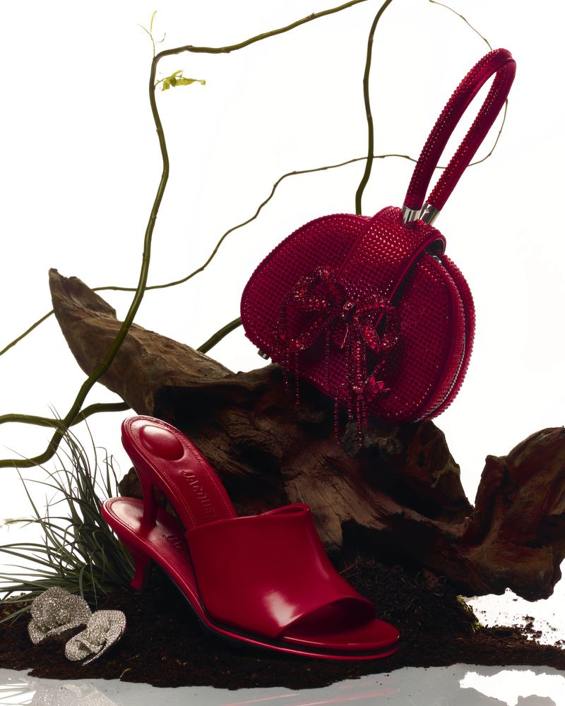 Elevated studio shot of a red high-heel mule and beaded handbag on a wood base against white, exuding luxury fashion.