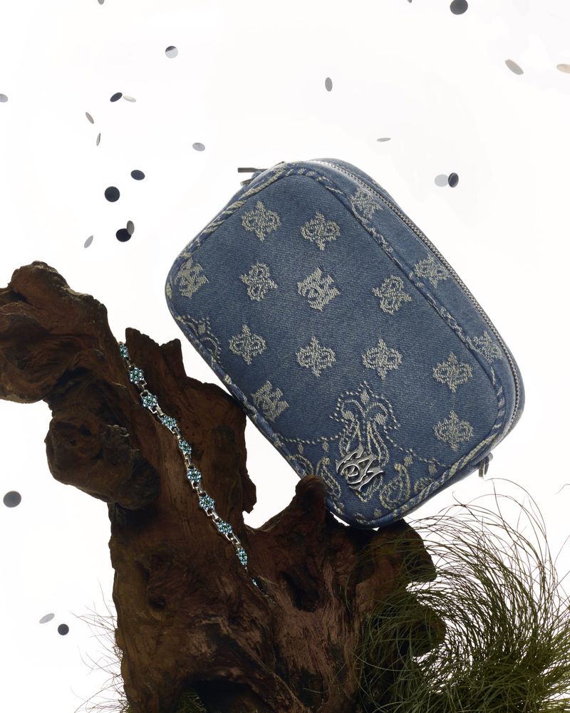 Denim cosmetic bag with a floral pattern rests on driftwood and ornamental grass against a white backdrop with confetti.