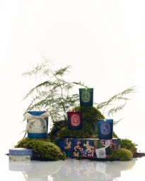 Collection of scented candles nestled in moss and foliage with a holiday gift box against a white background.