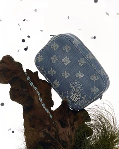 Monogram denim cosmetic pouch resting on a rustic piece of dark wood with scattered confetti against a clean white backdrop.