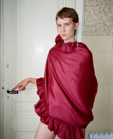 Young woman in a red ruffled dress poses in front of a white door and floral wallpaper, captured in a medium, eye-level studio shot.