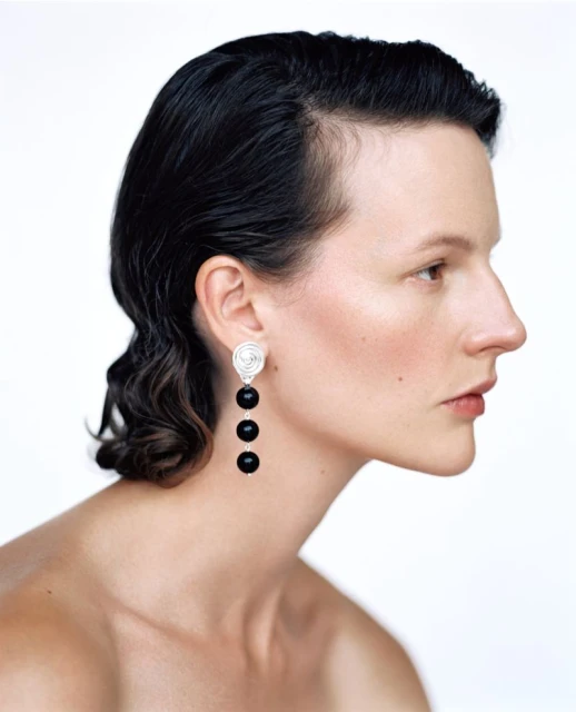 Profile portrait of a woman with dark hair and statement earrings against a clean white background. Beauty and fashion concept.