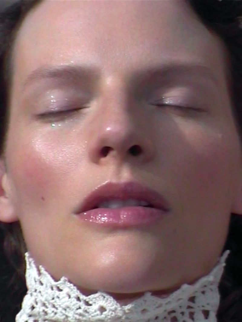 Closeup of a woman's face with her eyes closed, dewy skin, and a lace collar, emphasizing natural light and serene aesthetic.