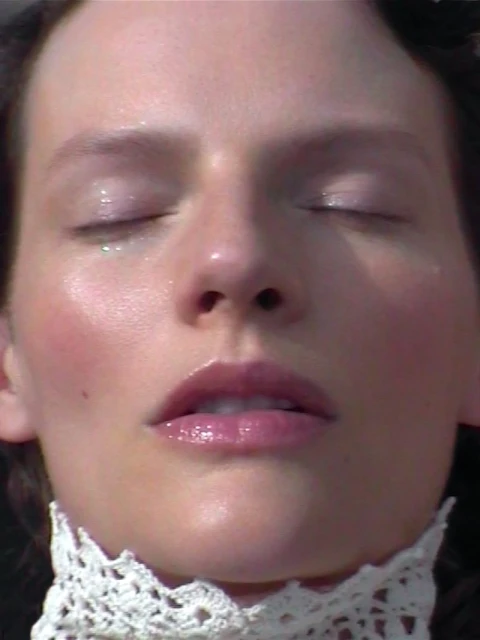 Closeup of a woman's face with her eyes closed, dewy skin, and a lace collar, emphasizing natural light and serene aesthetic. 