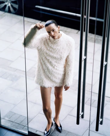 Sara Blomqvist in a white fringed textured mini dress standing outside glass doors for Beauty Projects Issue 2