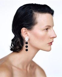Profile portrait of model Sara Blomqvist with slicked dark hair wearing a tiered black bead drop earring against a white background.