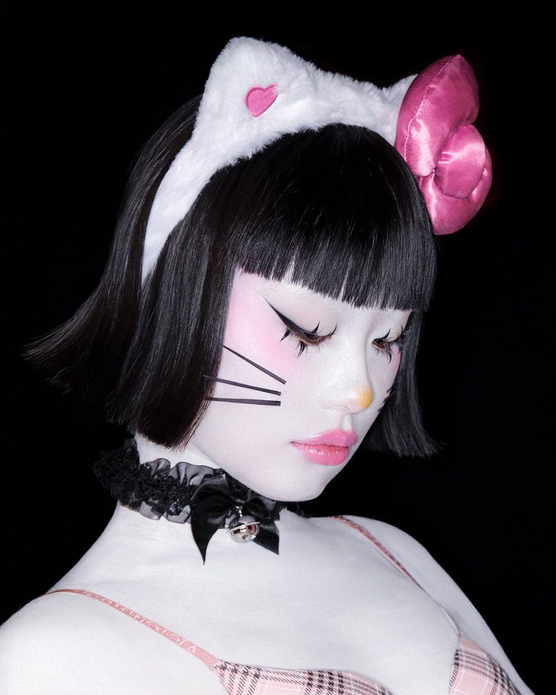 Young woman with artistic body paint and cat-ear headband poses against a dark background in a close-up studio portrait. 