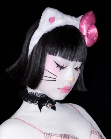 Young woman with artistic body paint and cat-ear headband poses against a dark background in a close-up studio portrait. 
