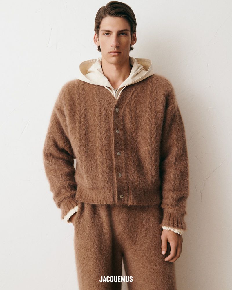 Male fashion model poses in brown knit cardigan and pants against off-white backdrop, showcasing the Jacquemus design and soft textures.