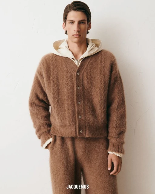 Male fashion model poses in brown knit cardigan and pants against off-white backdrop, showcasing the Jacquemus design and soft textures.
