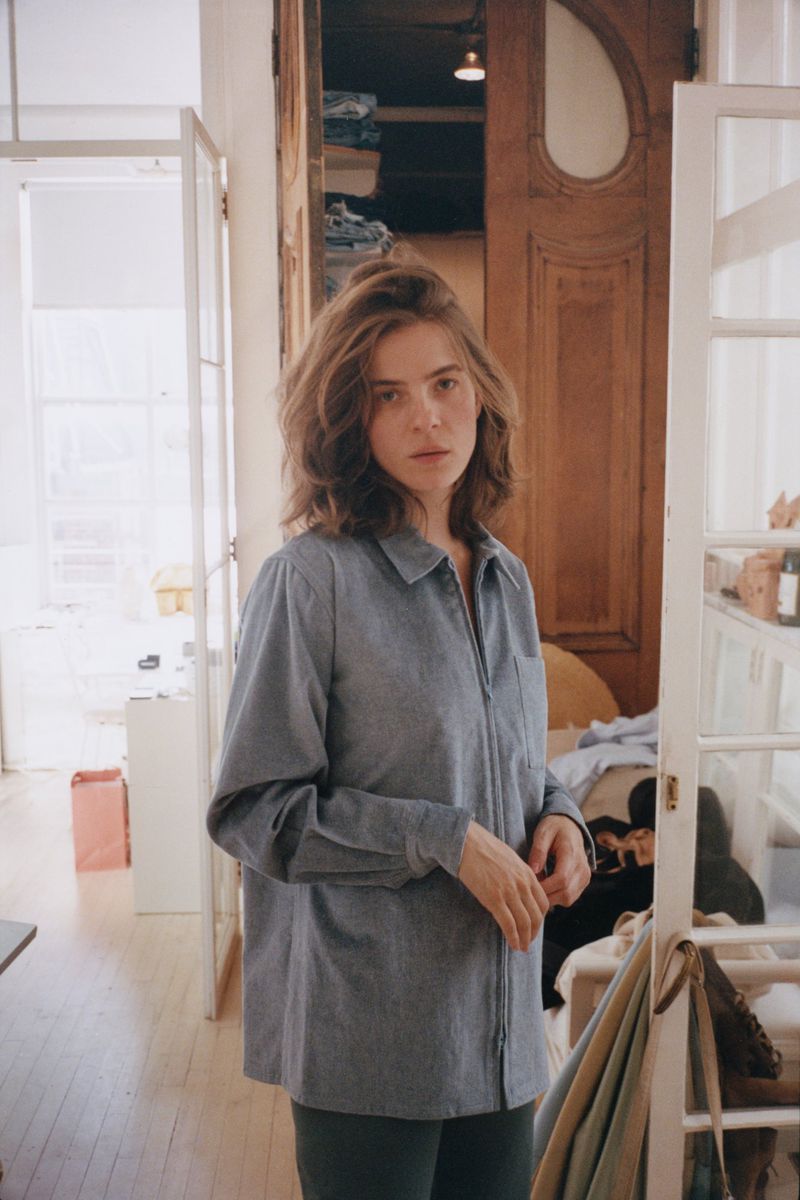 Woman in blue collared zip-up shirt standing indoors in a room with white doors and wooden architecture