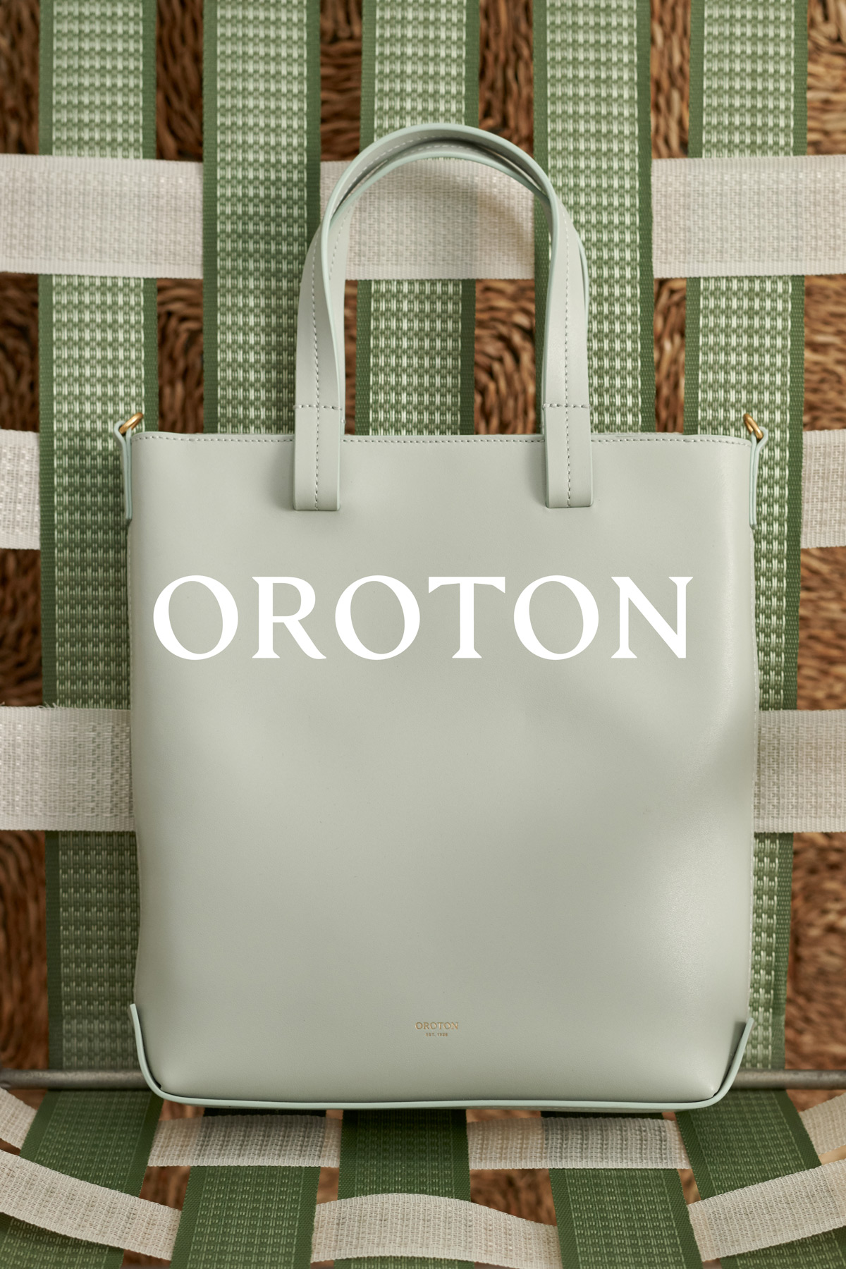 Light green Oroton tote bag with double handles and gold hardware sits on a patterned chair. Brand logo visible on the bag.