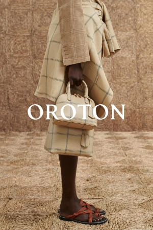 Model holding two matching beige plaid handbags wearing a plaid skirt and brown sandals against textured backdrop