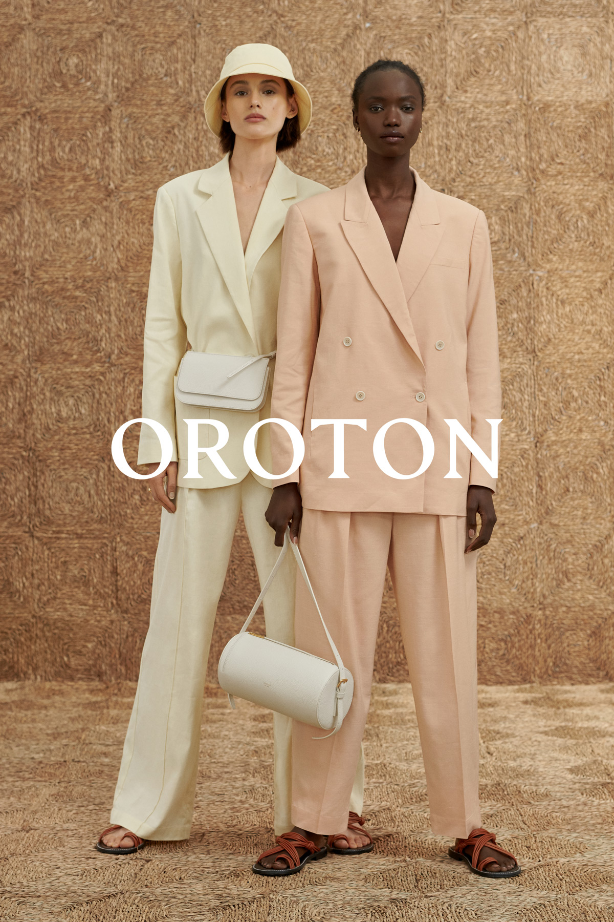 Two women model neutral-toned suits and handbags against a textured backdrop, showcasing fashion in a studio setting with soft lighting.
