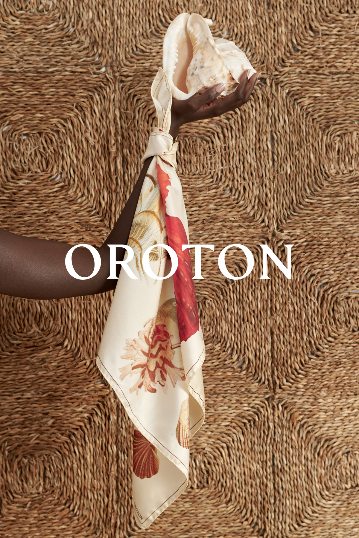 Dark-skinned hand holds a shell tied with a patterned scarf against a woven wall; Oroton text overlay at center.