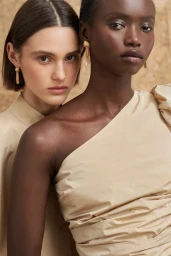 Two female models wearing beige tops and gold earrings against a textured background for Oroton summer campaign