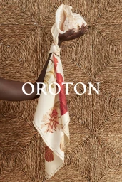 Hand holding a conch shell with a patterned silk scarf draped down against a woven textured background