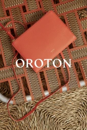 Orange leather shoulder bag resting on a woven wicker or rattan textured surface with brand text overlay
