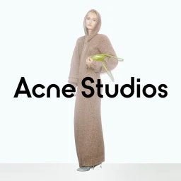Model in a long brown hooded knit dress holding a small lime green bag against a plain white studio background.