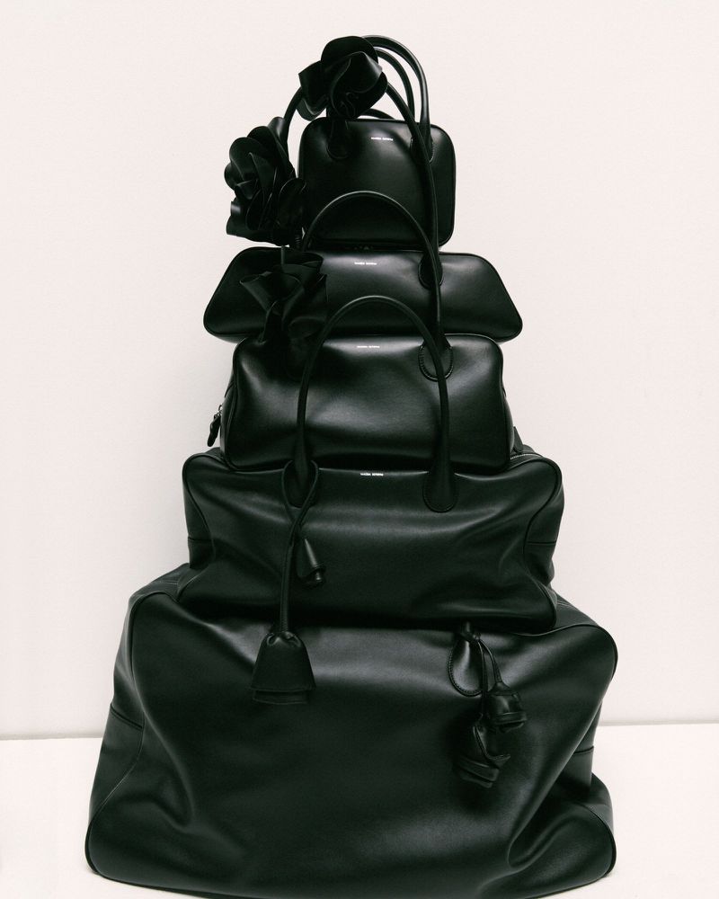 Stack of black leather handbags of varying sizes, arranged in a tower on a neutral background, accessorized with floral accents.