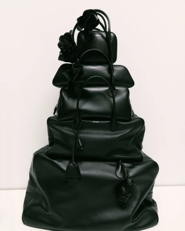 Stack of black leather handbags of varying sizes, arranged in a tower on a neutral background, accessorized with floral accents.