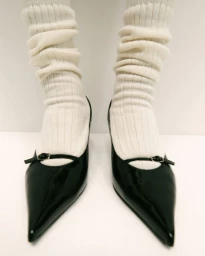 Close up of feet wearing black pointed toe heels and white ribbed knit socks against a seamless white background