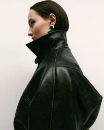 Profile portrait of a woman wearing a high-collared black leather jacket against a plain white background