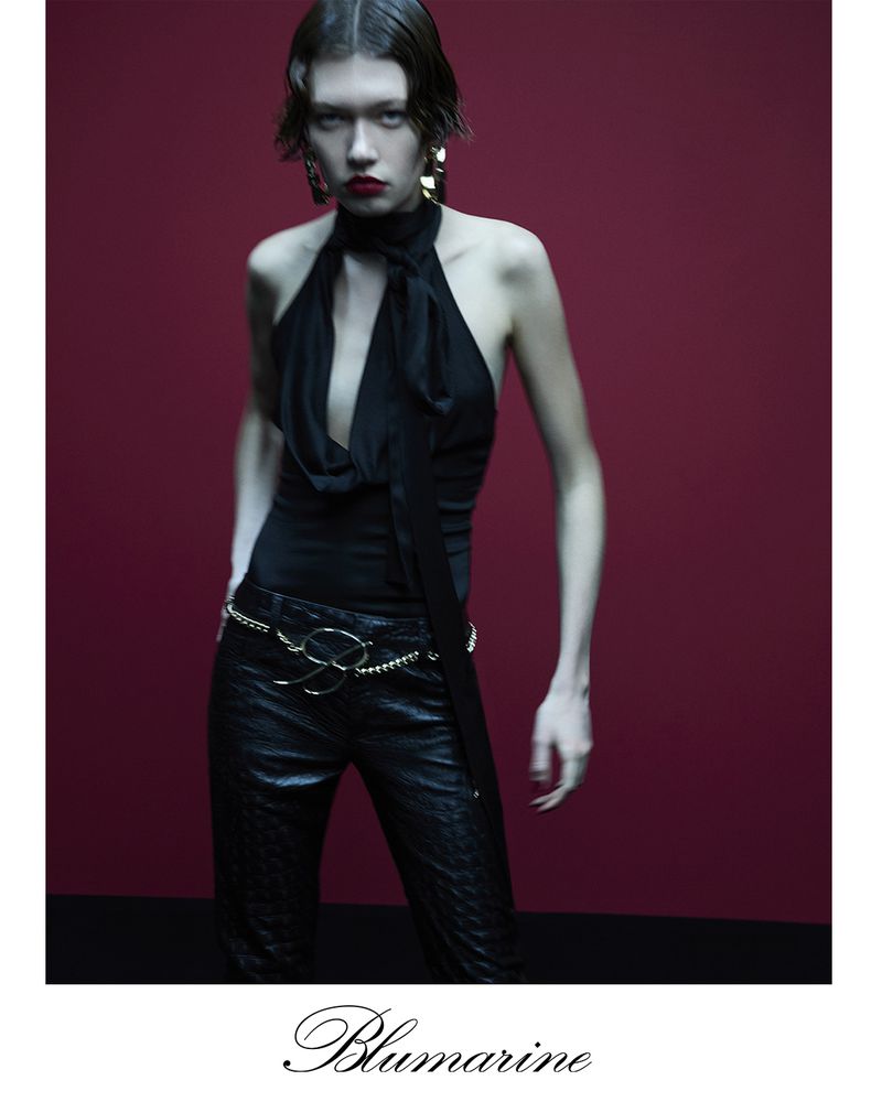 A striking fashion shot showcases a model in a black halter top and pants against a red background, highlighting contemporary style.