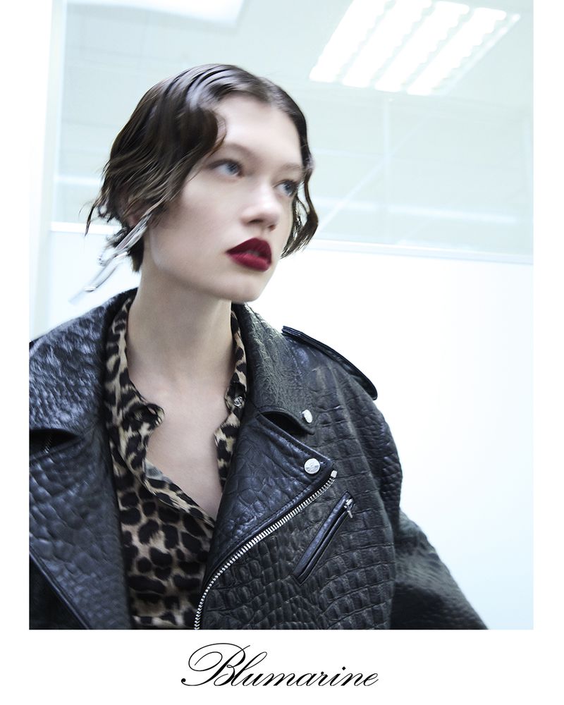 Brunette model in a glossy bob hairstyle and dark red lips wears a reptile print jacket and animal print blouse in a studio shot.