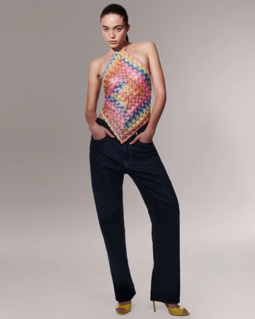 Model wearing a colorful patterned halter top and dark denim jeans against a grey seamless studio backdrop