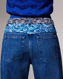 Close-up shot of blue denim jeans with a patterned waistband and a blue textured knit top against a seamless background