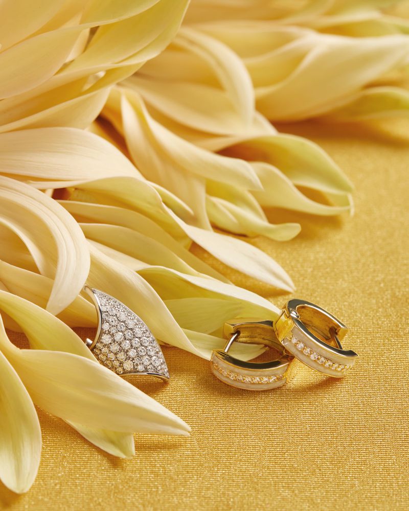 Close-up of gold and white earrings and a pendant on petals with a gold fabric background, luxury jewelry, soft diffused light.